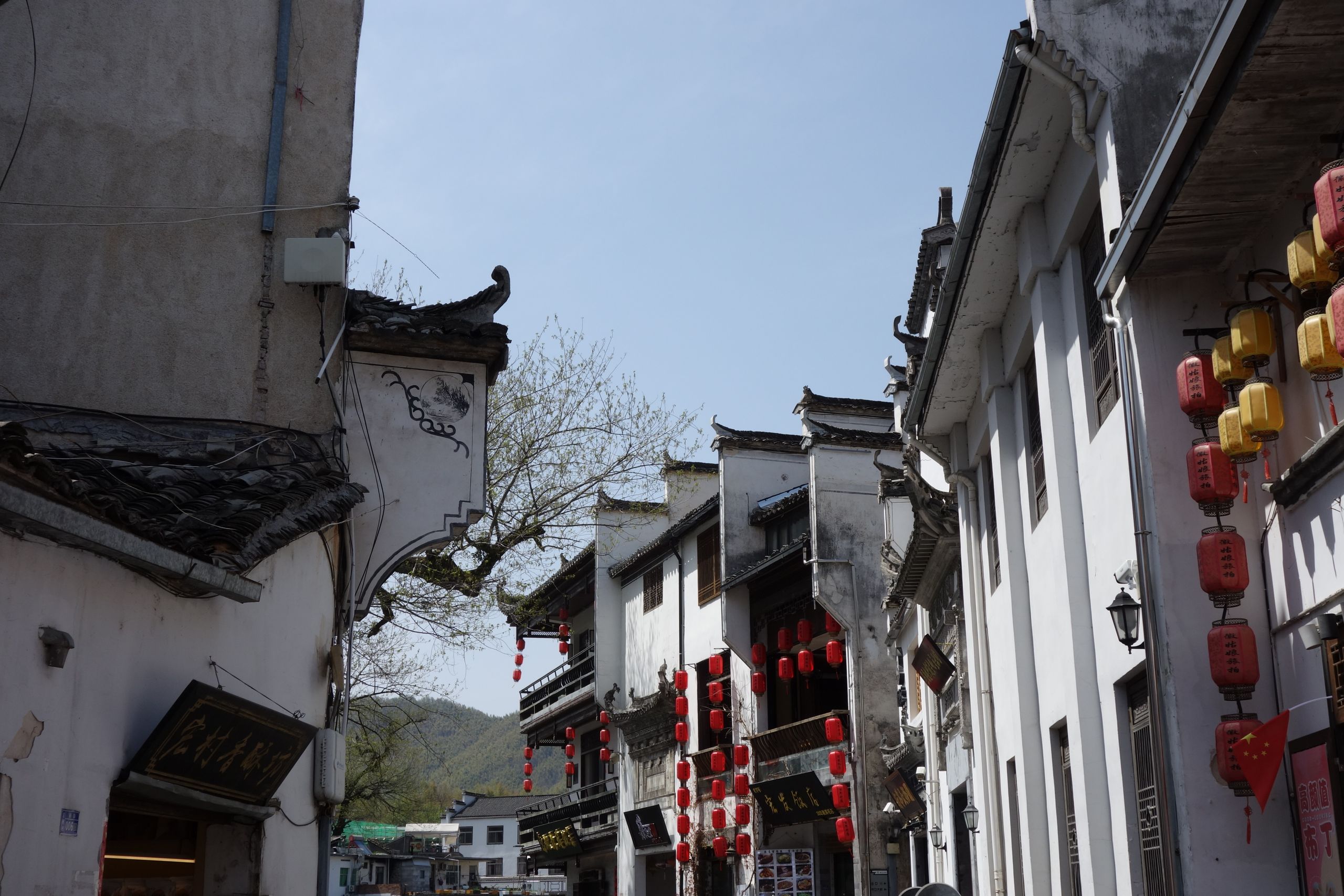 Quaint street in traditional Chinese architecture with red lanterns under a clear blue sky.
